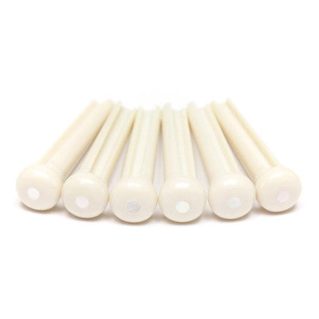 Six white guitar bridge pins with small white pearl-like dots on top arranged in a row on a white background.