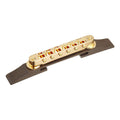 Gold-colored Tune-O-Matic style guitar bridge mounted on a dark wood base viewed at an angled perspective.