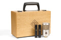 Wooden carrying case with two small black microphones and one larger silver microphone with mesh grille.