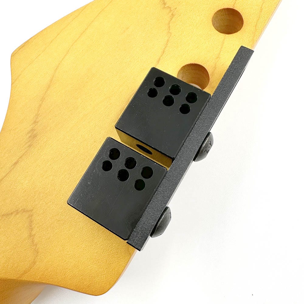 Black machine head pin drill locator tool attached to light brown wooden guitar headstock with drill guide holes.