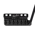 Black Vega Trem guitar bridge with six string saddles and a tremolo arm attached on the right side.
